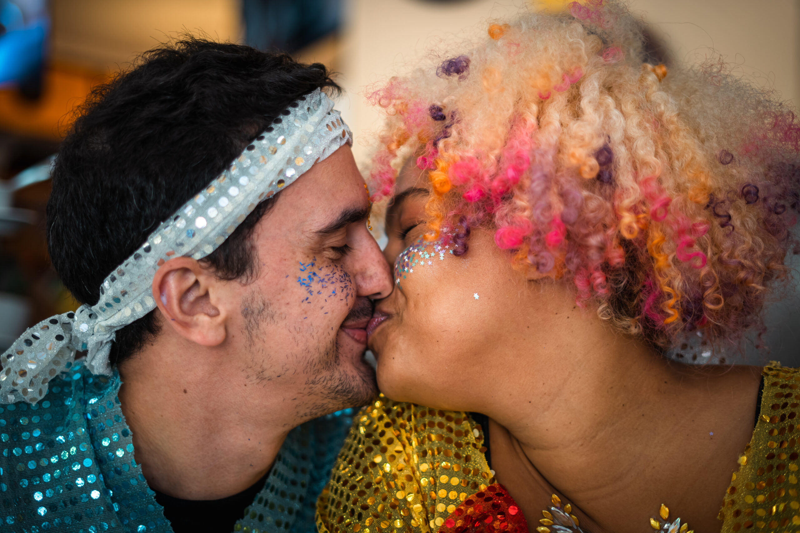 Couple kissing. He's a white man and she's a black girl with very colored curly hair. They are both wearing sparkling clothes