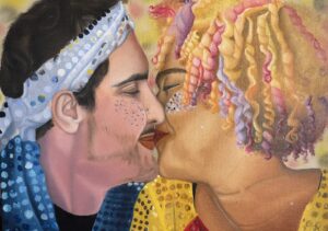 Casal se beijando. Ele é um homem branco com uma roupa azul com paetês e ela é uma mulher negra, de cabelos loiros e coloridos, usando uma roupa dourada e vermelha com paetês e glitter no rosto.