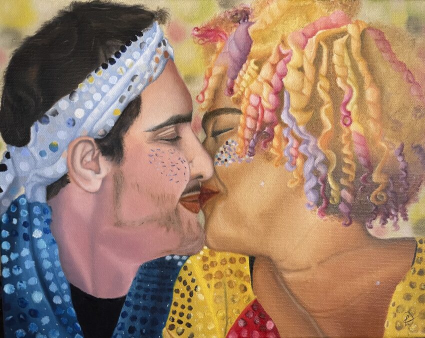 Casal se beijando. Ele é um homem branco com uma roupa azul com paetês e ela é uma mulher negra, de cabelos loiros e coloridos, usando uma roupa dourada e vermelha com paetês e glitter no rosto.