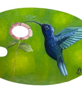 Paleta de tinta de madeira com uma pintura em cima. O desenho é um beija-flor pegando o nectar de uma flor cor de rosa, sendo que o furo da paleta é a parte de dentro da flor