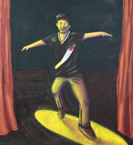 Chico está em um palco com um foco de luz amarela sobre ele. Ele dança com os braços abertos e usa uma camisa do Vasco